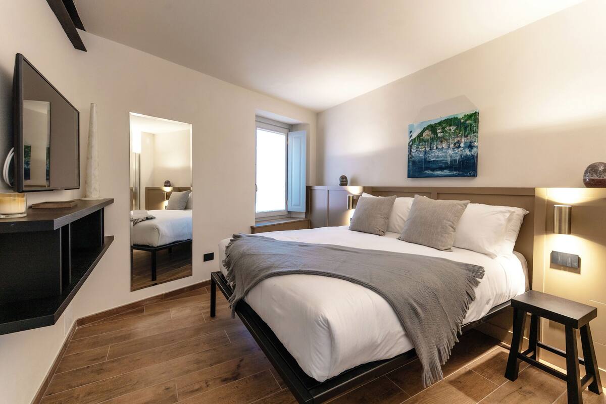 Une chambre à coucher moderne avec un grand lit, des tables de chevet, un miroir et un tableau au mur.