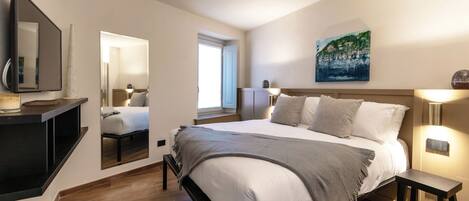 A modern bedroom with a large bed, bedside tables, a mirror, and a painting on the wall.