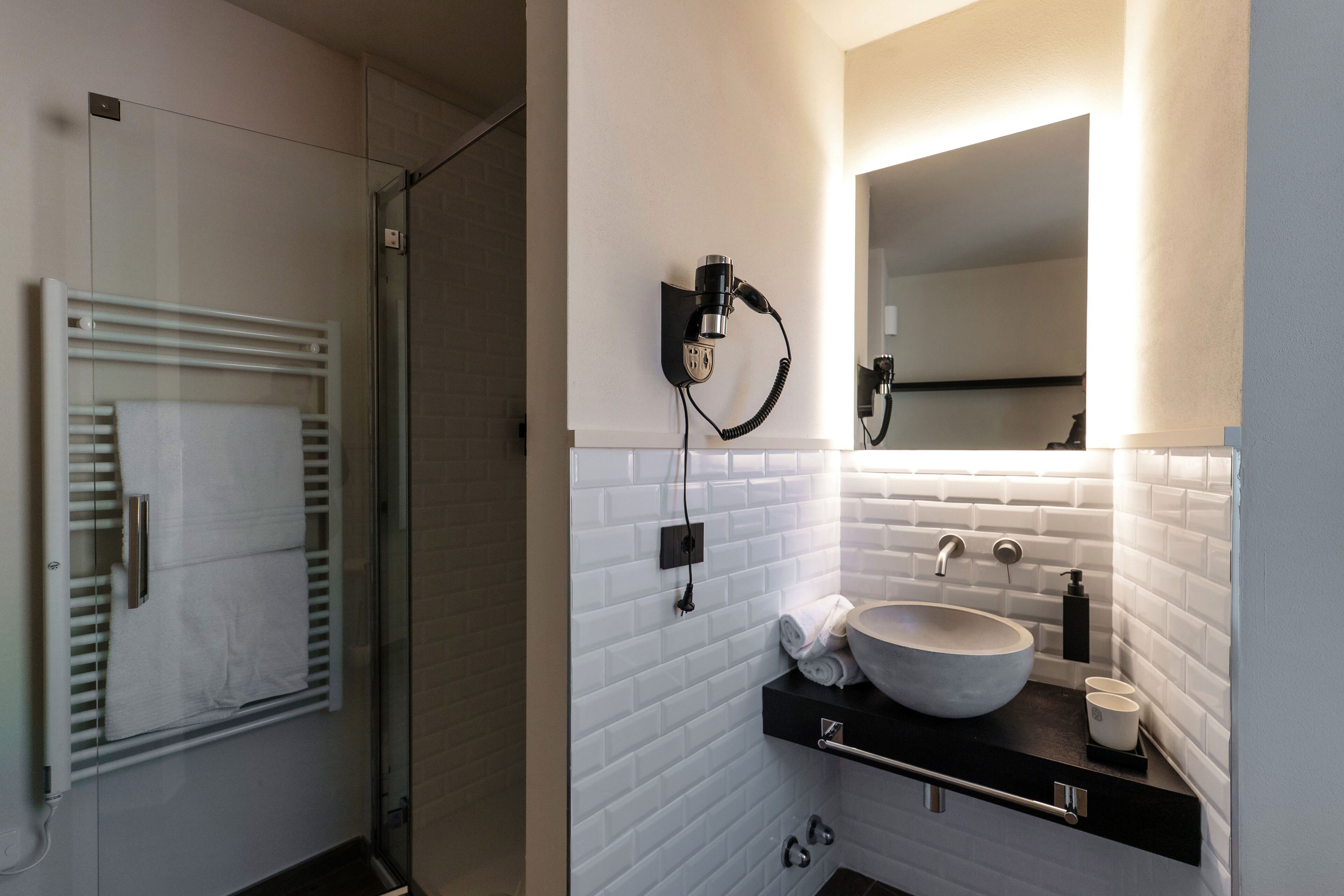 Een moderne badkamer met een douchecabine van glas, een witte betegelde wand, een groot wastafel met een waskom en een zwart aanrecht.