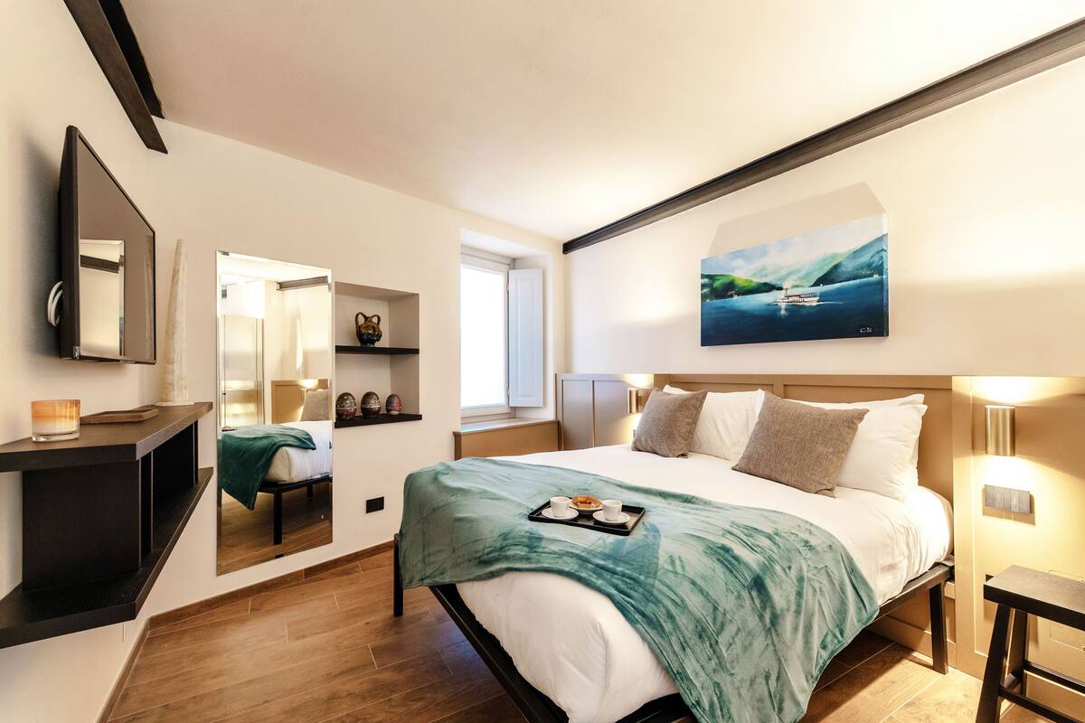 Une chambre d’hôtel moderne avec un grand lit, une table de chevet, un miroir, un tableau et une fenêtre.