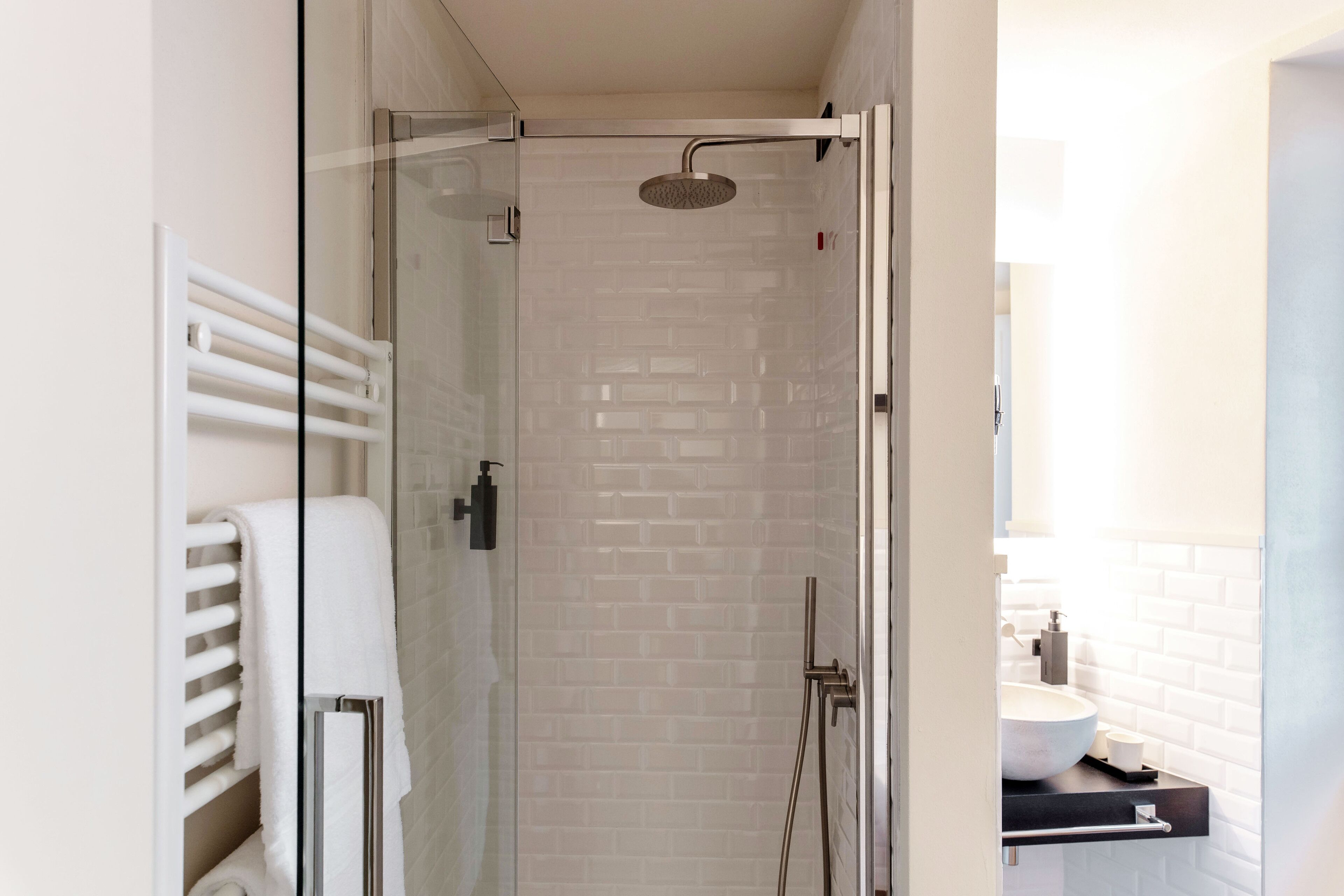 A modern bathroom with a glass-enclosed shower, white tiled walls, and a visible towel rack.