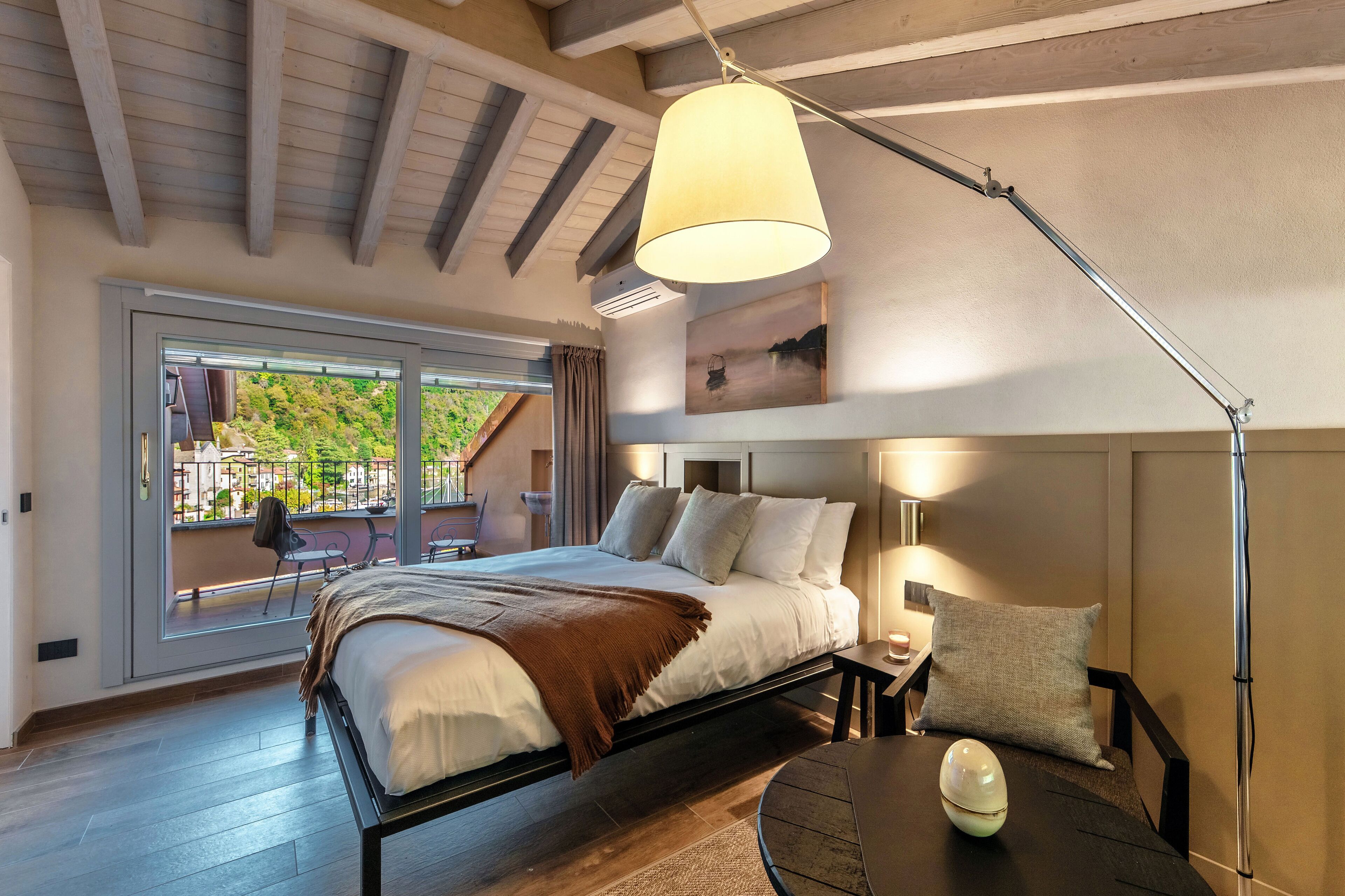 Une chambre moderne avec un grand lit, une table de chevet, une lampe et une vue sur l’extérieur grâce à une porte coulissante.