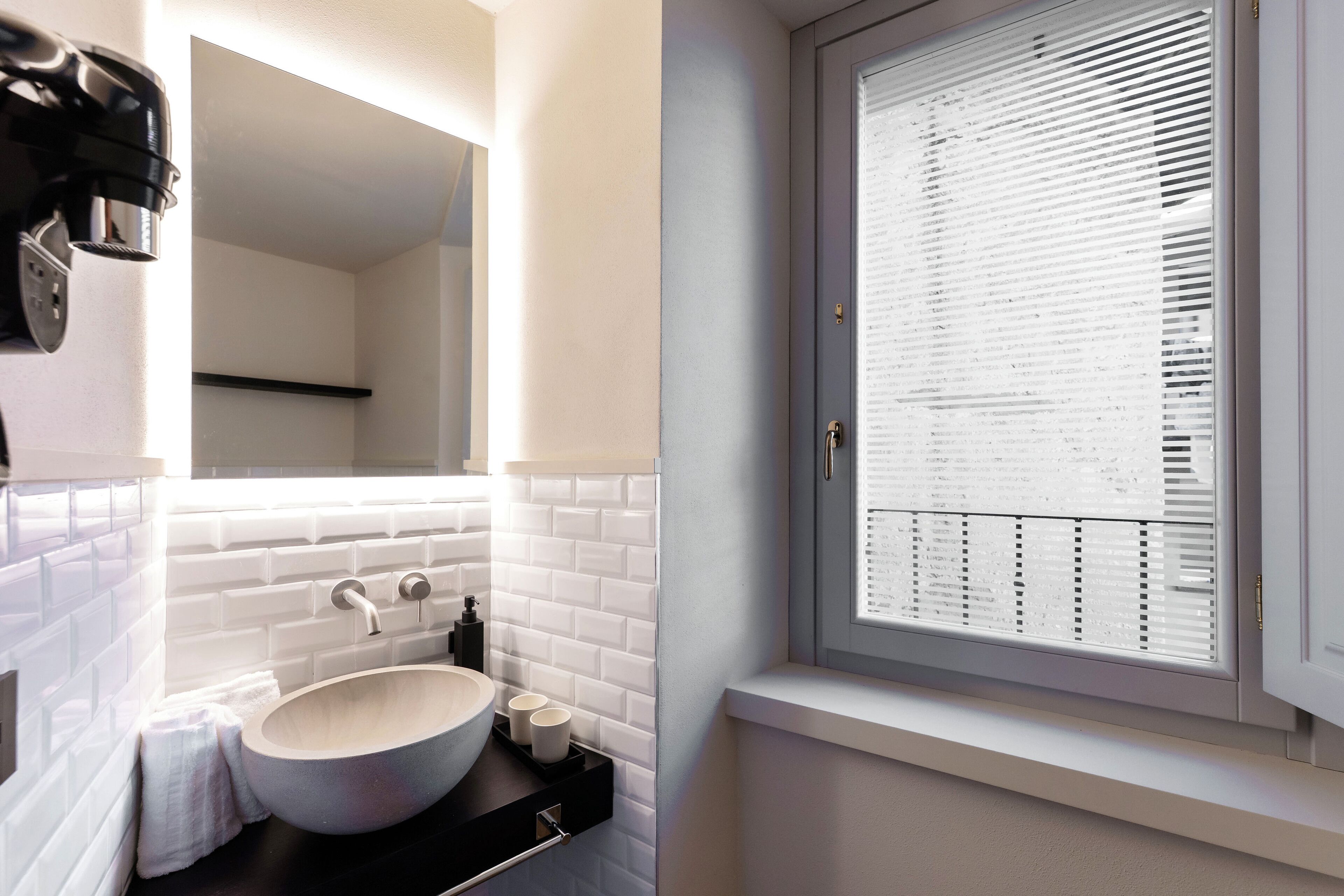 A bathroom with a white sink, a mirror, and a window with blinds.