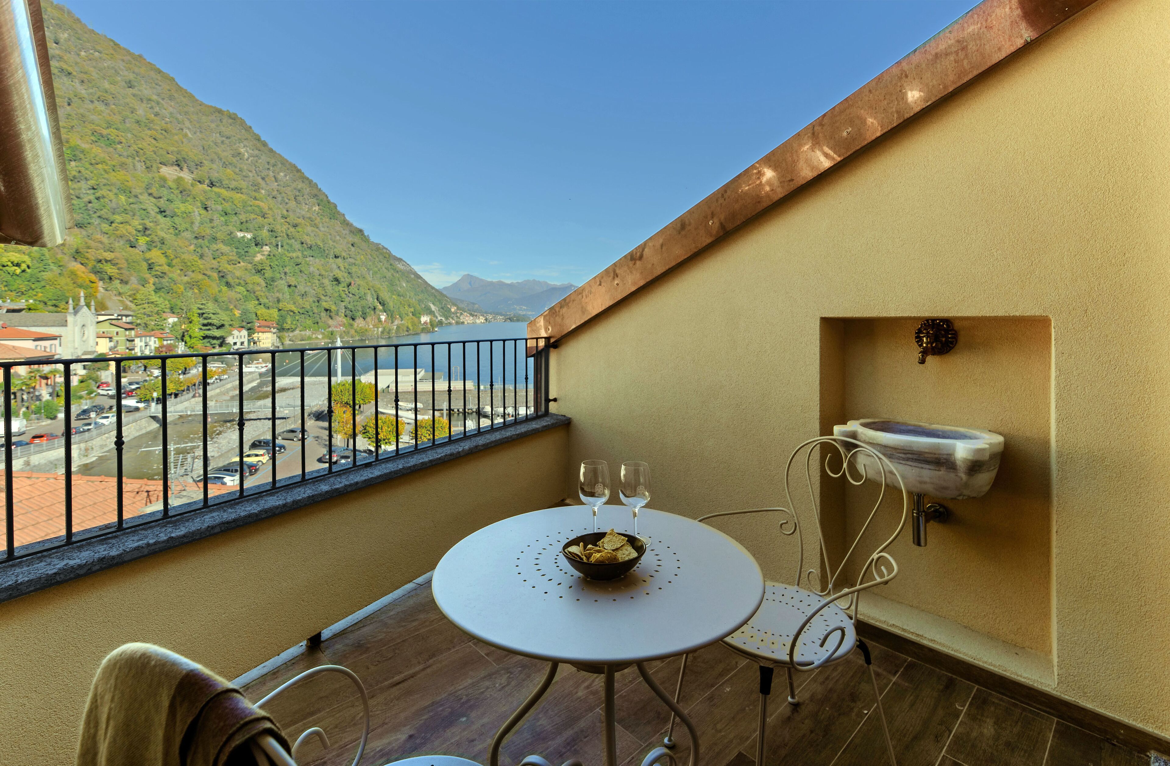 A balcony with a table, two chairs, a bowl of chips, and two wine glasses.