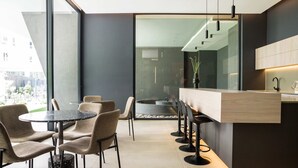 Un interior moderno con una mesa redonda y sillas, una zona de bar con taburetes, y vistas a través de un muro de cristal.
