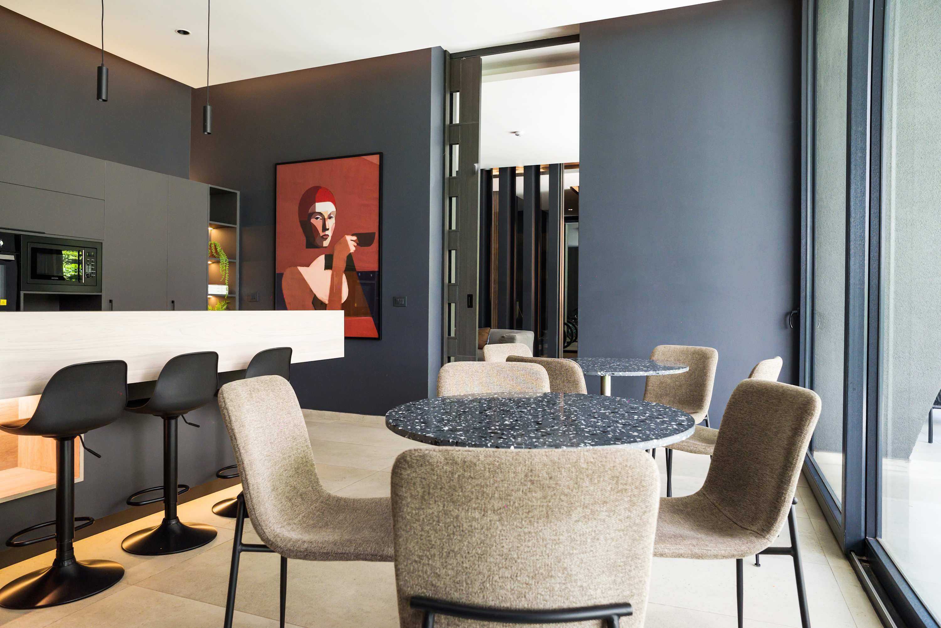 A modern bar area with bar stools, round tables, and a large abstract painting on the wall.