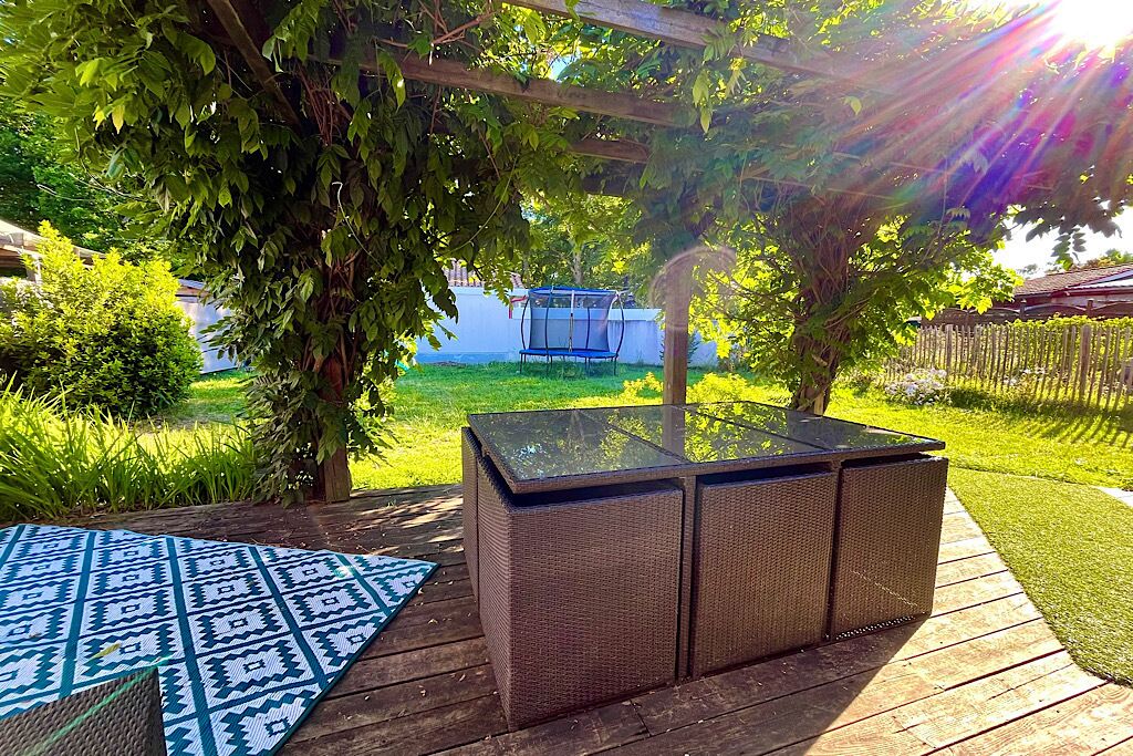 A patio area with a glass-top table and wicker chairs, surrounded by greenery and a swing set.