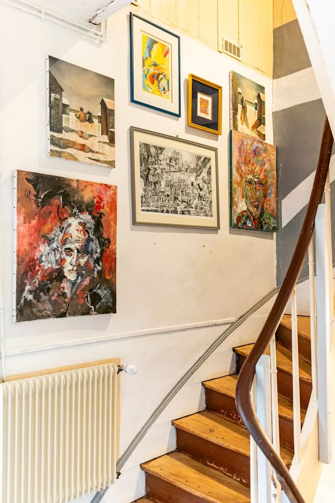 Un escalier avec une rampe en bois et des murs blancs ornés d’œuvres d’art encadrées.
