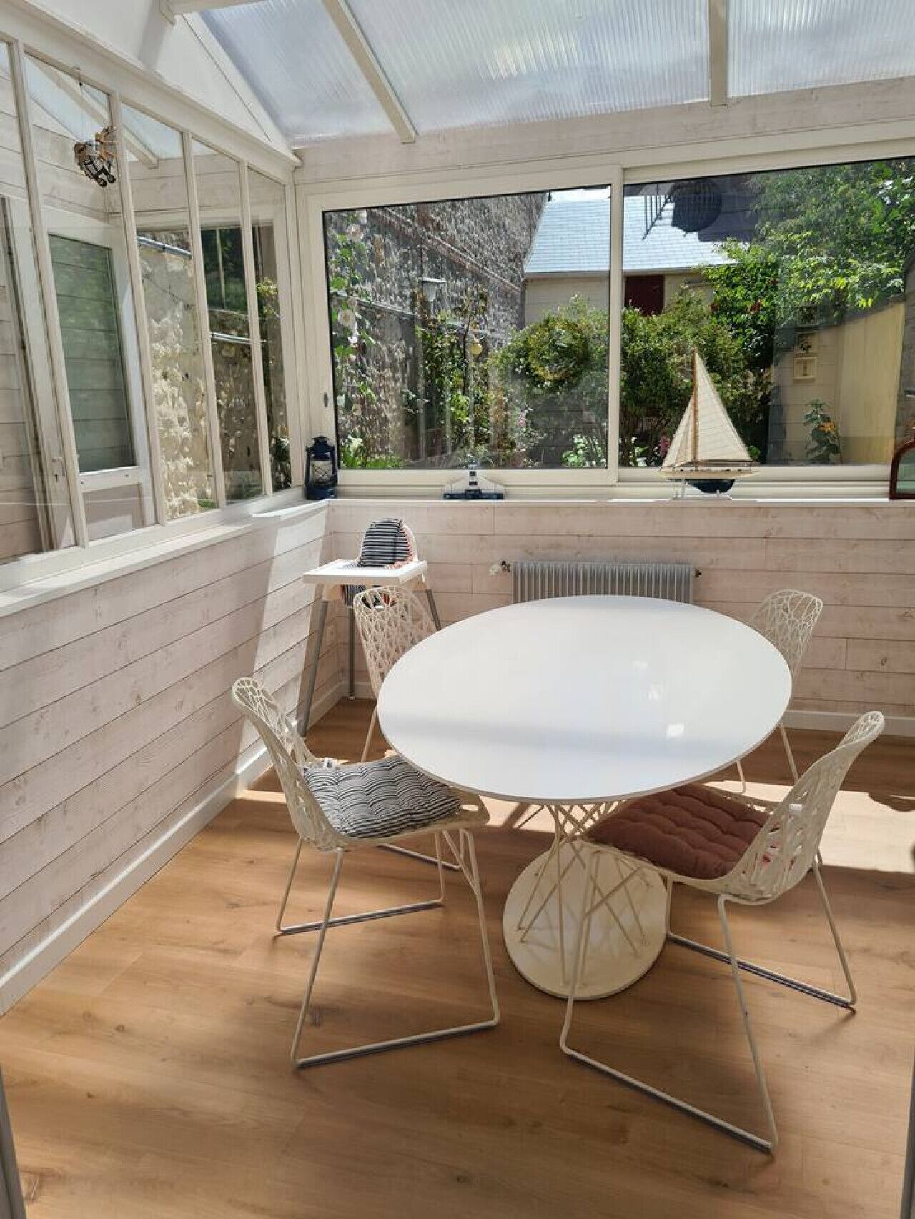 A conservatory with a round table and chairs, large windows, and a view of greenery outside.