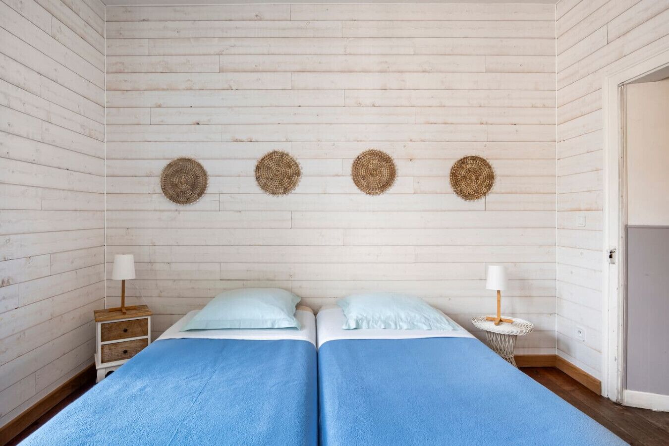 A room with two beds, a wooden wall, and three woven wall hangings.