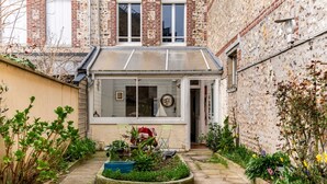 Un patio estrecho con un pequeño jardín, una puerta que da a una habitación y un muro de ladrillo.