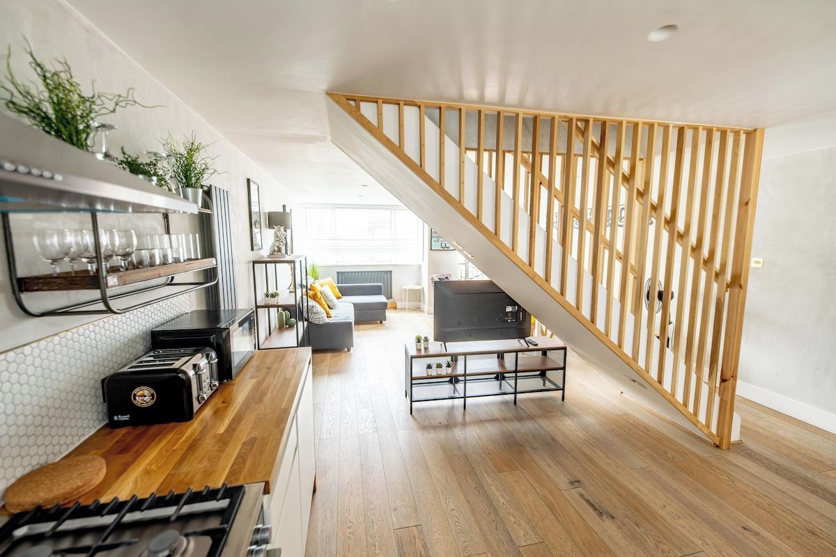 A modern kitchen with a wooden staircase, a dining area, and a living room with a TV.