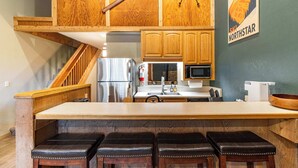 Une cuisine dotée de meubles en bois, d’un réfrigérateur en acier inoxydable, d’un four à micro-ondes et d’un comptoir-bar en bois avec des tabourets.
