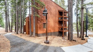 Une cabane en rondins moderne dotée d’un balcon, entourée de grands pins.