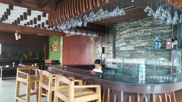 Un espace bar avec des chaises en bois, un comptoir en verre et des lampes suspendues.