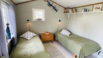 Ett rum med två sängar, ett litet bord, en hylla med böcker och ett fönster.