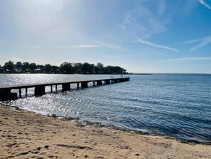 En brygga som sträcker sig ut i stilla vatten, med en sandstrand i förgrunden.