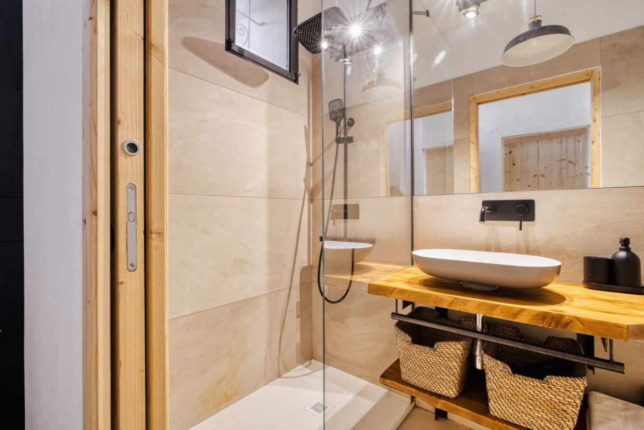 Ein modernes Badezimmer mit einer Duschkabine aus Glas, einem Holzausziehtisch mit einem großen Waschbecken und einem Spiegel darüber.
