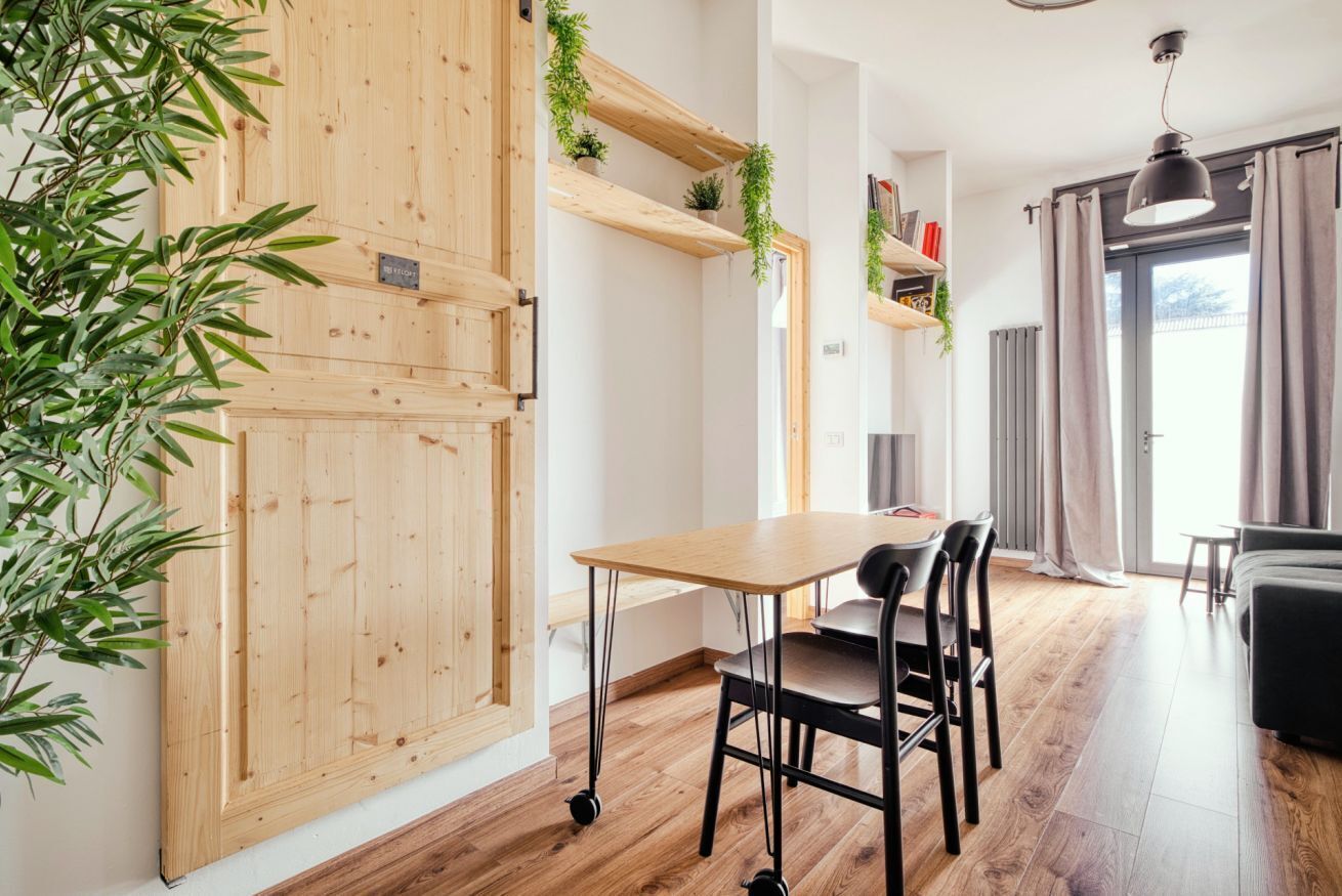 Une pièce avec une porte en bois, une table entourée de chaises, un luminaire suspendu et une plante.