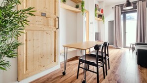 Una habitación con puerta de madera, una mesa con sillas, una lámpara colgante y una planta.