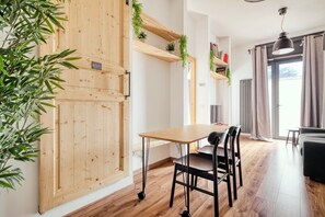 Ein Zimmer mit Holztür, Tisch mit Stühlen, einer Pendelleuchte und einer Pflanze.