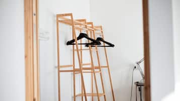 A room with a wooden wardrobe, a desk with a lamp, and a hanging rack with clothes.