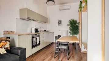 A compact kitchen with a dining area, wooden flooring, and a black pendant light.