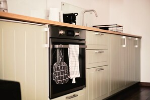 Una cocina con horno empotrado, cafetera y un tendedero con un paño.