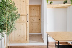 Una puerta de madera con un picaporte de metal, una mesita con un asiento negro, y una planta a la izquierda.