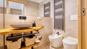 Un baño moderno con un espejo grande, tocador de madera, lavamanos blanco y un bidé.