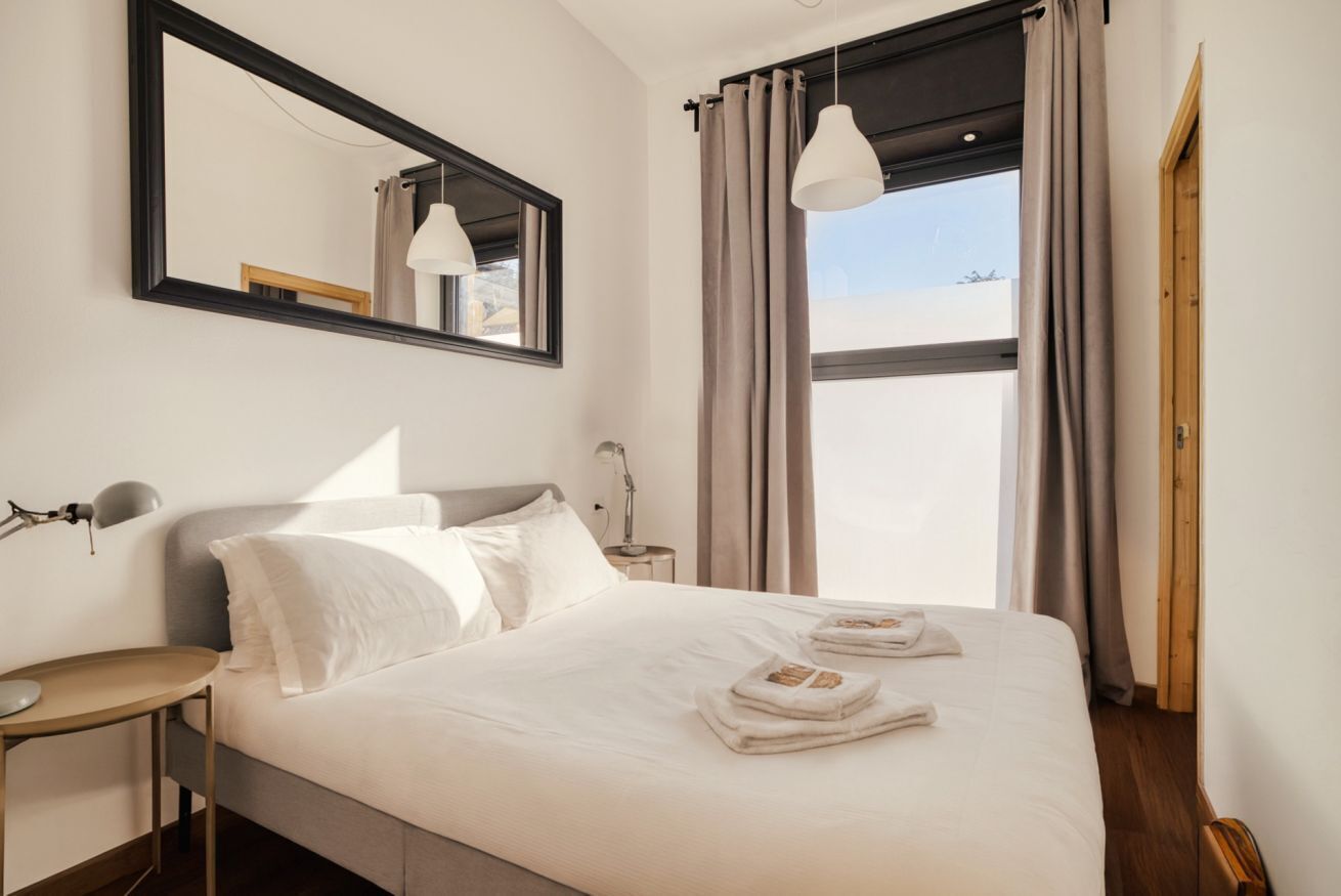 Habitación de hotel con cama, escritorio, espejo y ventana con cortinas.
