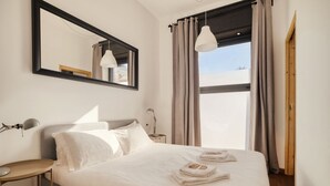 Habitación de hotel con cama, escritorio, espejo y ventana con cortinas.
