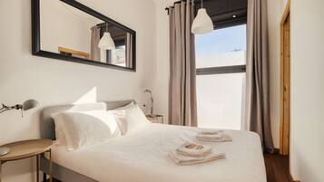 Habitación de hotel con cama, escritorio, espejo y ventana con cortinas.