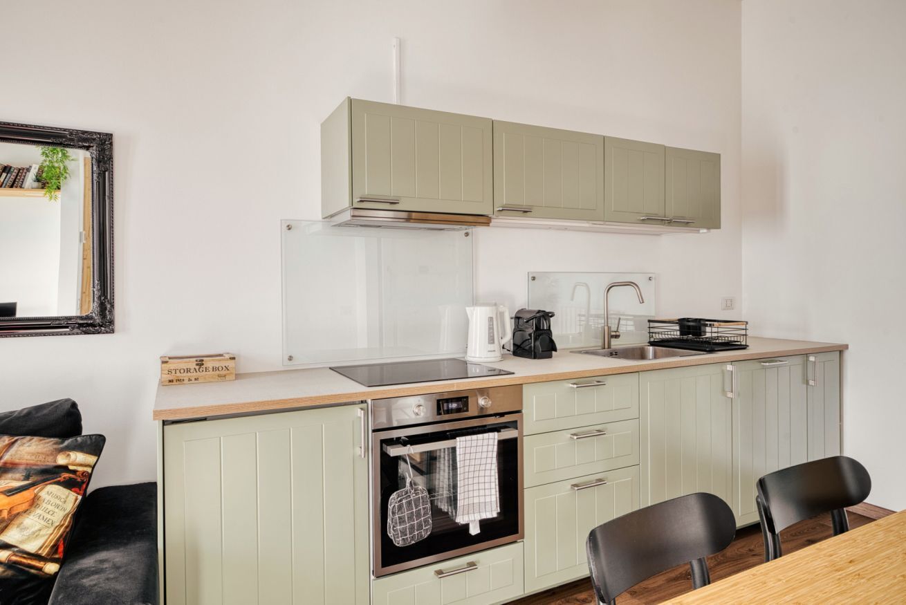 A compact kitchen with a built-in oven, a coffee maker, and a kettle on the countertop.