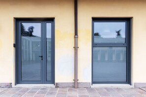 Un edificio con dos puertas, una ventana, una tubería visible y un acceso pavimentado.