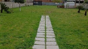 A pathway leading through a grassy area with a stone border, surrounded by a low wall and sparse vegetation. - Villa Pompeii Oasis (Torre Annunziata)