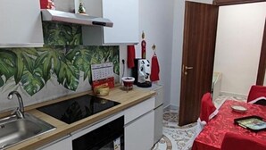 A compact kitchen with a sink, stove, and a calendar on the wall. There is a dining area with a table and chairs. - Villa Pompeii Oasis (Torre Annunziata)