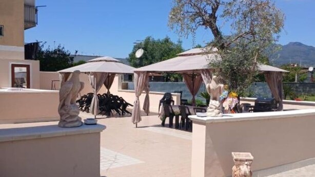 An outdoor seating area with umbrellas, a statue, and a table with a vase of flowers. - Villa Pompeii Oasis (Torre Annunziata)