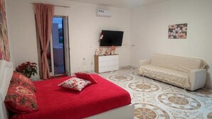 A bedroom with a bed, a white sofa, a TV, and a patterned floor. - Villa Pompeii Oasis (Torre Annunziata)