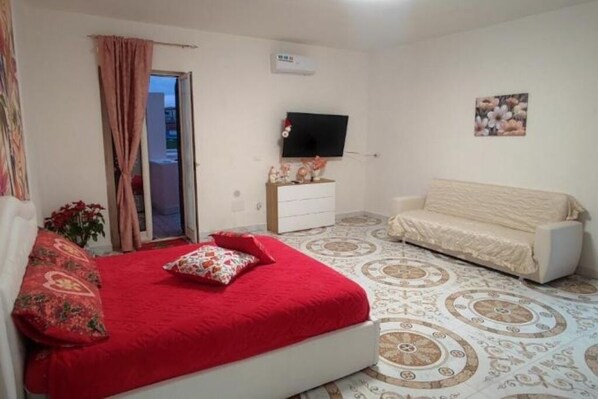 Un dormitorio con cama, un sofá blanco, televisión y suelo estampado.