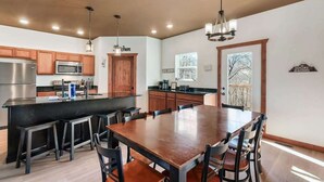 A modern kitchen with wooden cabinets, a large island with bar stools, a dining table with chairs, and pendant lighting. - Luxe Cabin, Sleeps 11, Sauna, Gym, Theater Game (Sevierville)