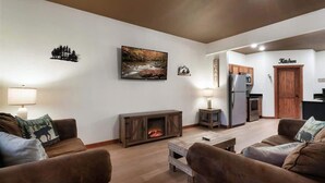A living room with a fireplace, a dining area, and a kitchen. - Luxe Cabin, Sleeps 11, Sauna, Gym, Theater Game (Sevierville)