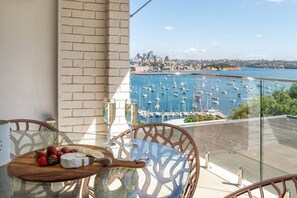 A balcony with a table set for two, a city skyline view, and a marina with boats. - Darling Point Apartment with Harbour Bridge Views (Darling Point)