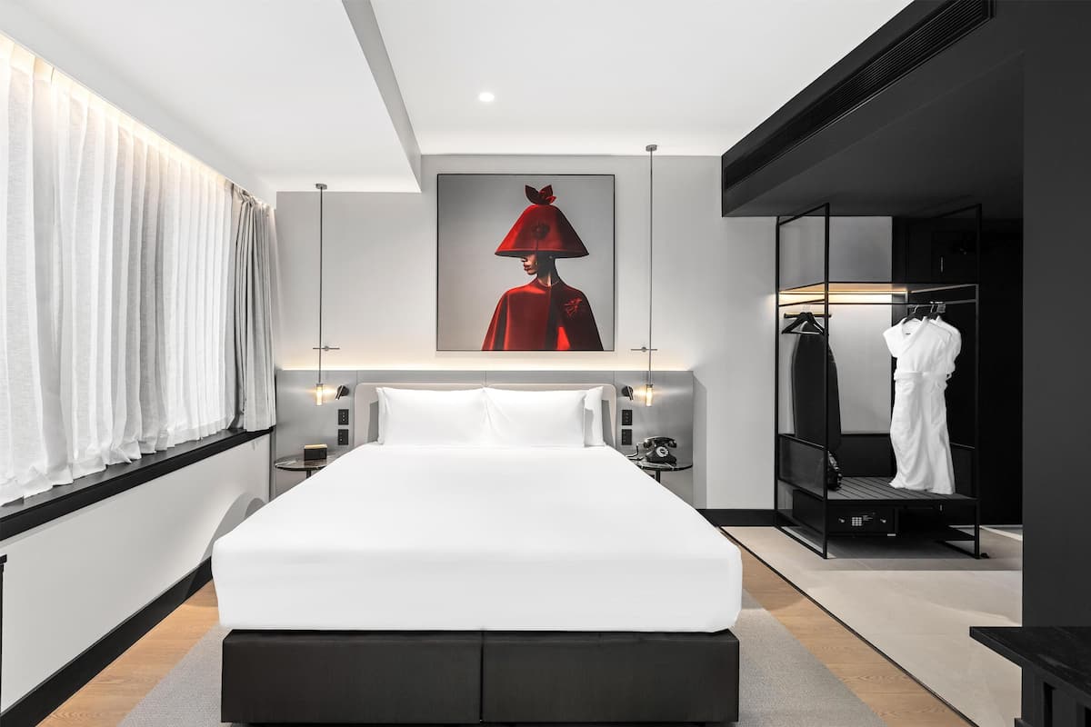 A modern hotel room with a large bed, a wardrobe, and a framed artwork on the wall.