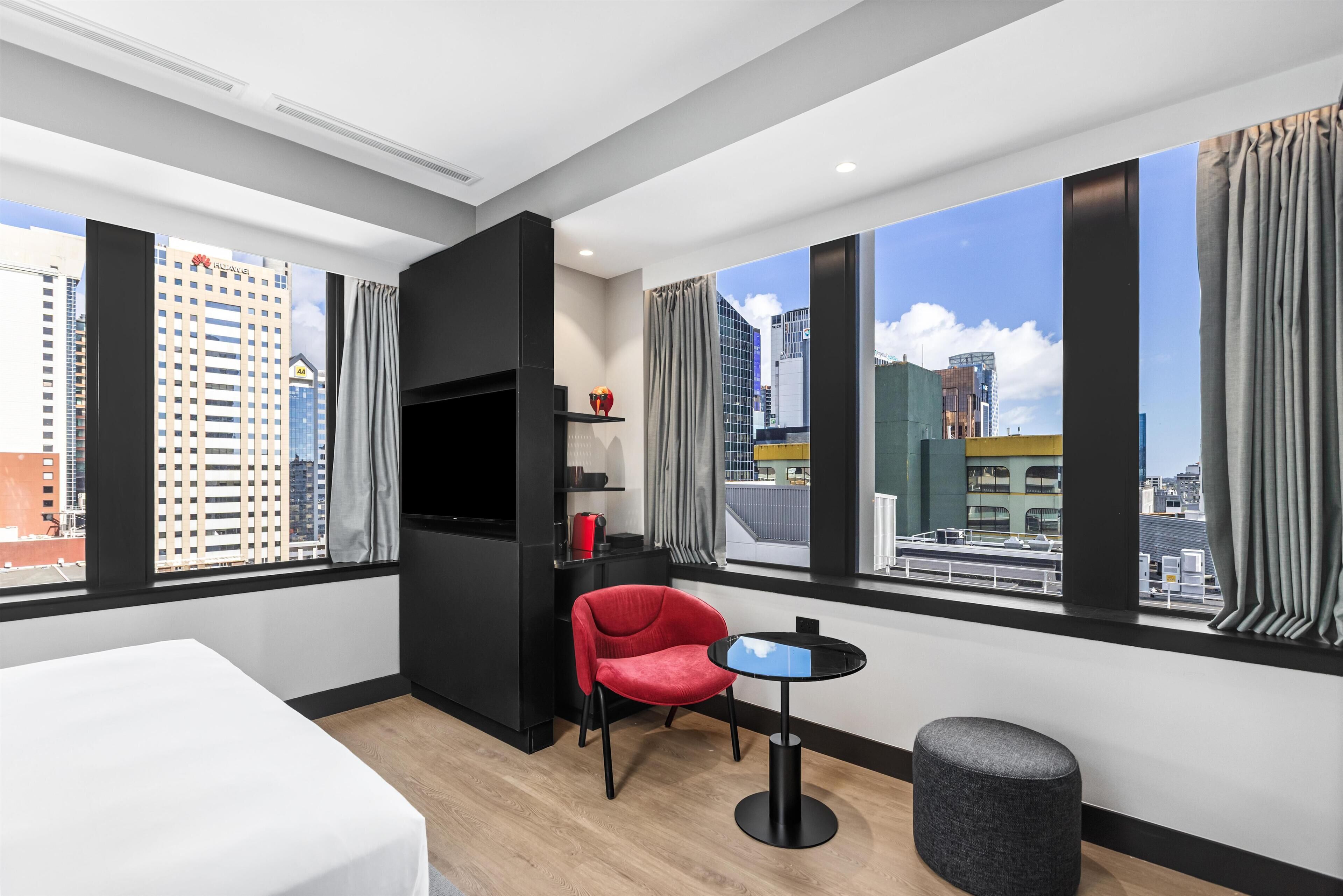 A modern hotel room with a bed, a red chair, a small table, and a TV.