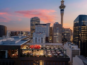 A modern building with a rooftop terrace featuring outdoor seating and a view of the city skyline, including a prominent tower.