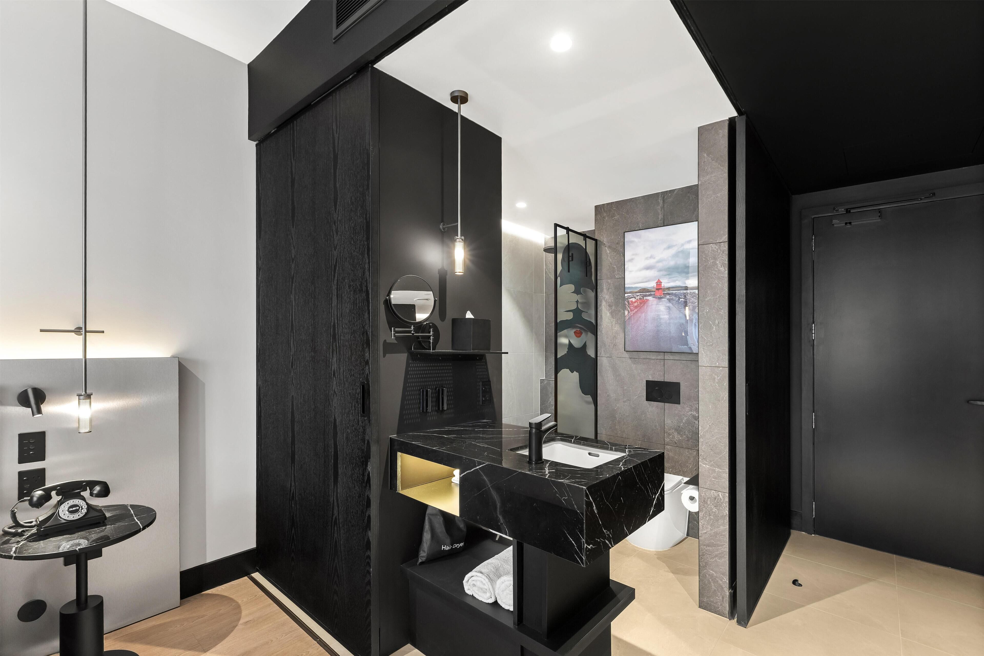 Un baño moderno con un tocador negro, un espejo redondo, un lavabo negro y un perchero para toallas.