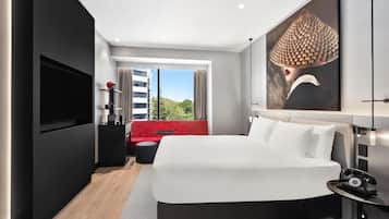 Habitación de hotel moderna con una cama grande, televisor de pantalla plana, sofá rojo y vista a la ciudad.
