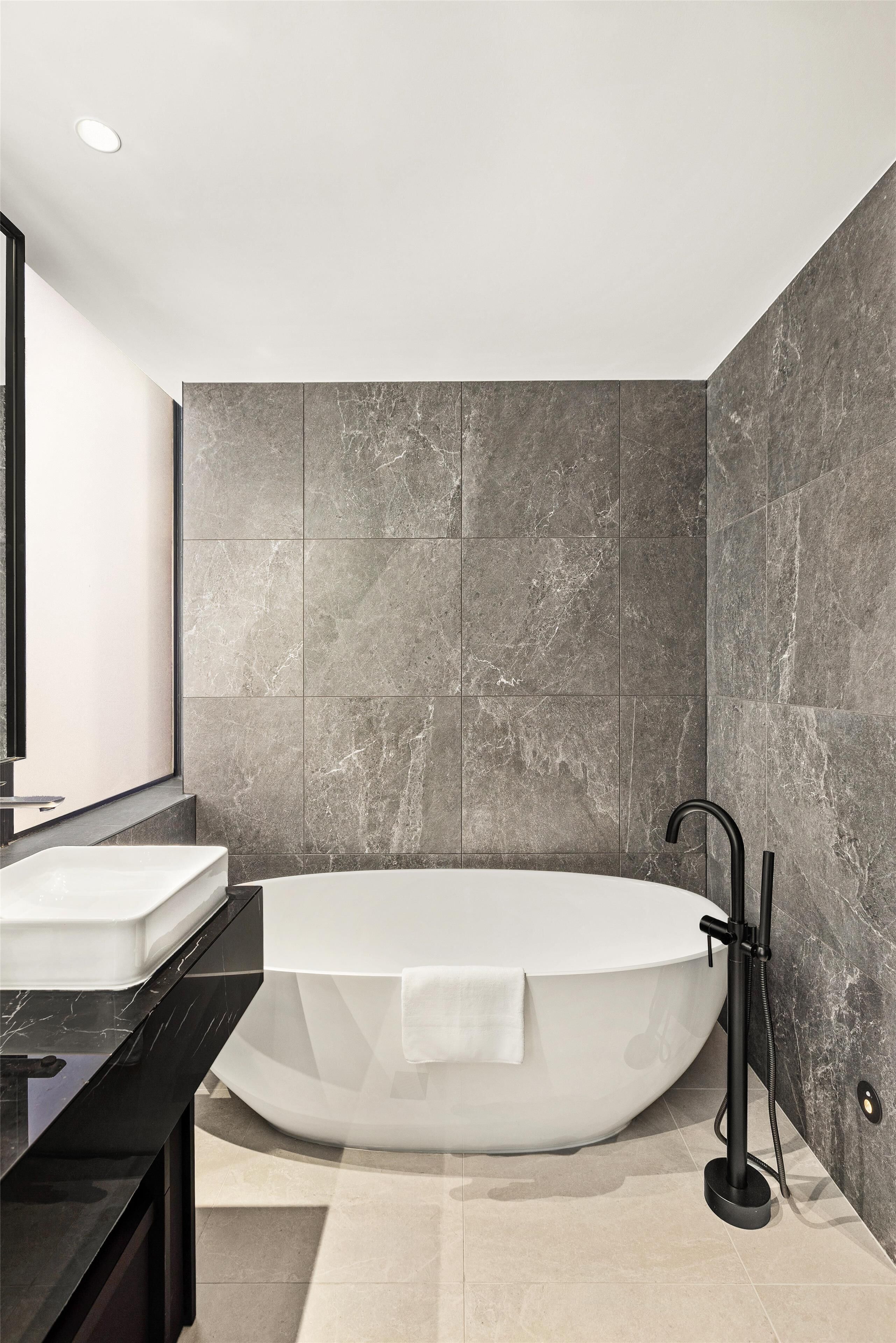 Ein modernes Badezimmer mit einer freistehenden Badewanne, einem großen Spiegel und einer schwarzen Ablagefläche.