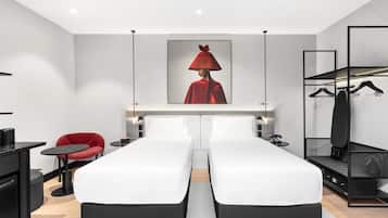 A modern hotel room with two beds, a red chair, a black desk, and a coat rack.